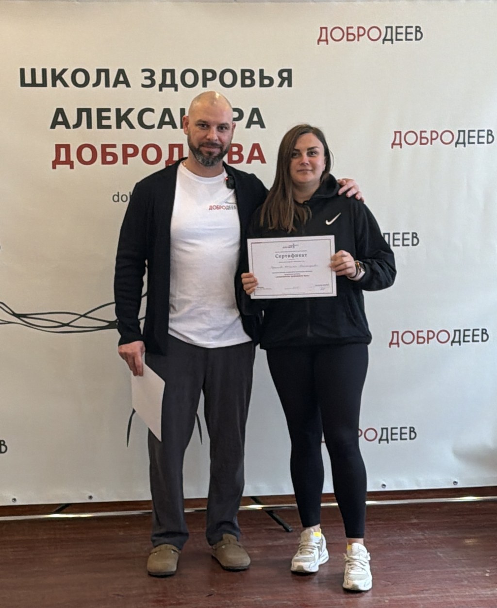 Александр Добродеев и участница обучения с сертификатом на фоне баннера «Школа здоровья Александра Добродеева»