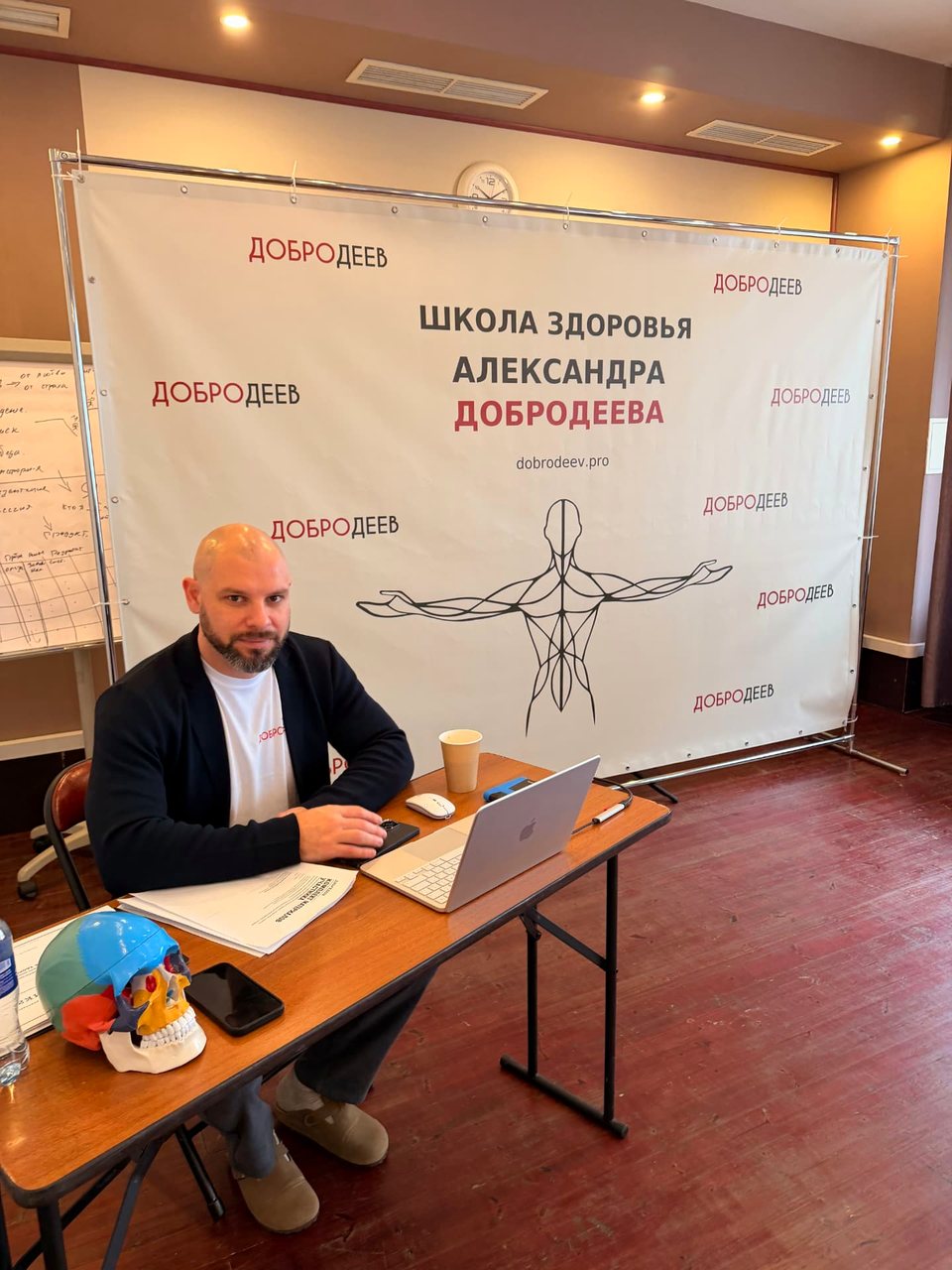 Александр Добродеев готовит занятие: учебные материалы, анатомическая модель черепа и ноутбук на столе
